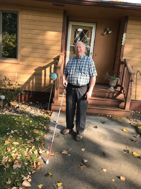 Allan Peterson, white can in hand, standing outside his house on the sidewalk.