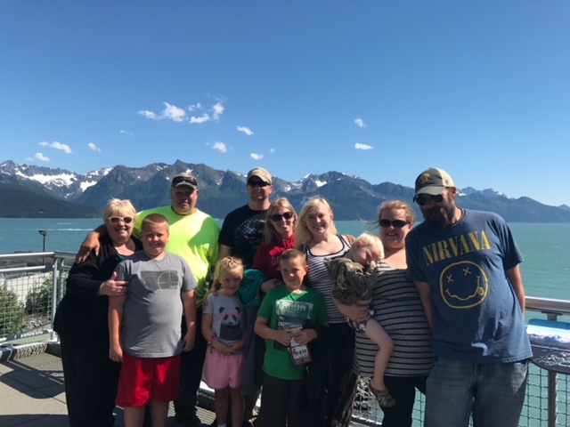 Pictured are Gerald's family with mountains in the background.  Lisa and Gerald are with daughter Kelsey and her family on the left. Kelsey and Ryan, they have Braven (14), Bridger (12), and Berlyn (11). Daughter Heather and her family on the right. Heather and Travis, they have Shelby (21) and Derek (7). 
