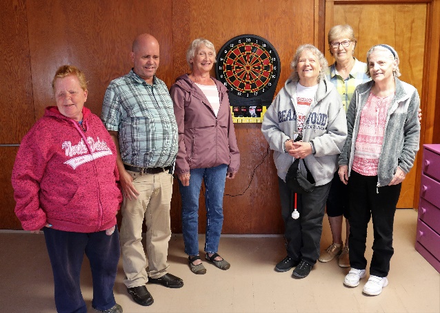 Camp Photo: Shirley, Bobbi, Carol, Mary, Susan, and Rosie are standing in front of the Audible Electronic Dartboard