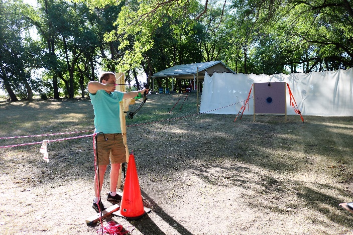 Nick is standing with bow drawn at the archery range.  He is ready to let the arrow fly towards the target.