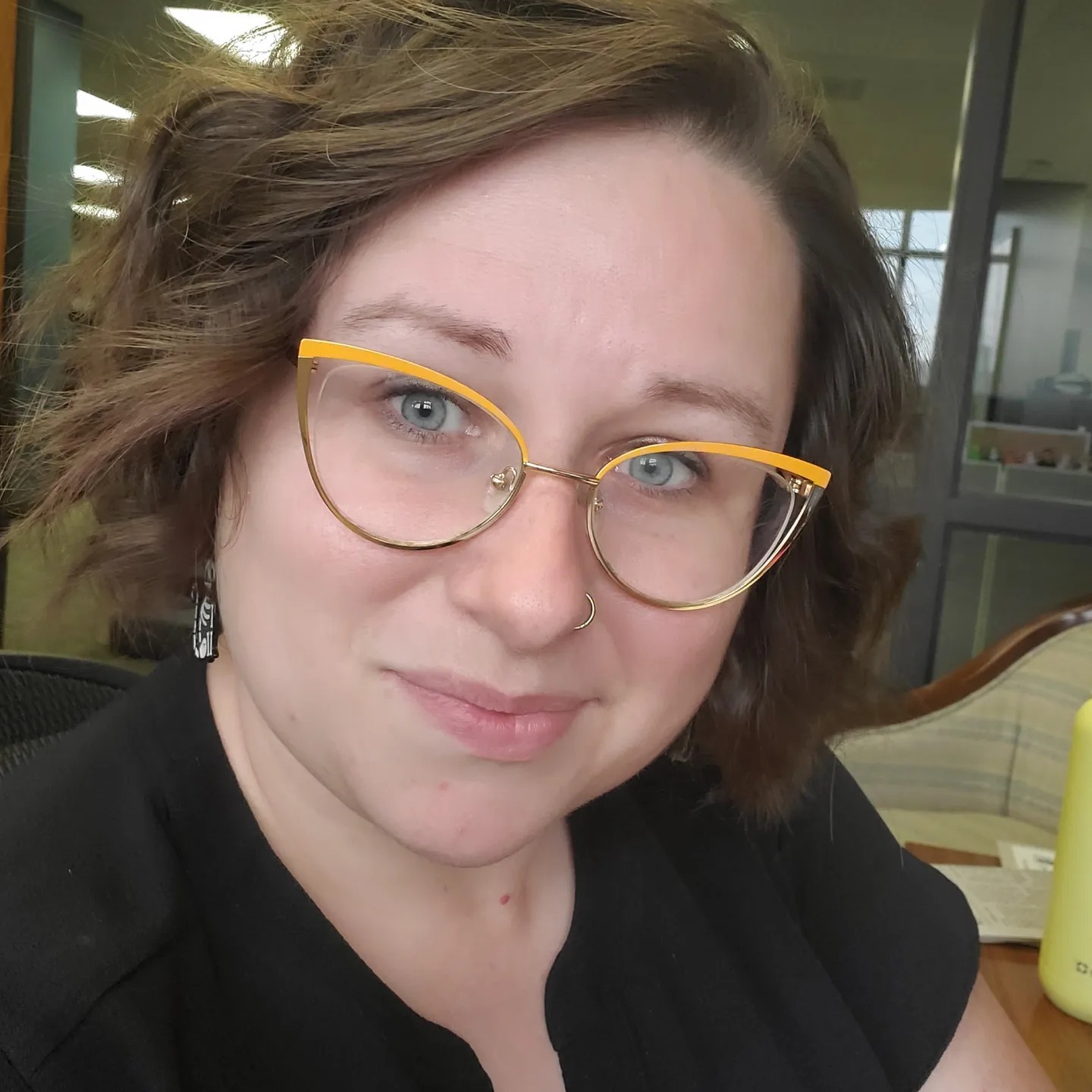 Kaity has short, curly brown hair and yellow cat-eye glasses.